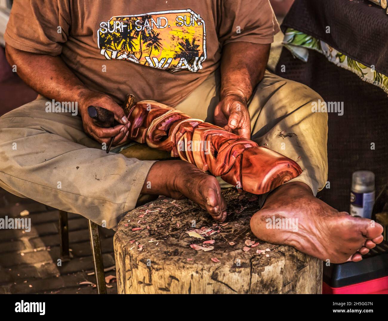 Un homme hawaïen s'assoit pieds nus et sculptera du bois avec un outil pour créer un artisanat traditionnel; Maui, Hawaii, États-Unis d'Amérique Banque D'Images