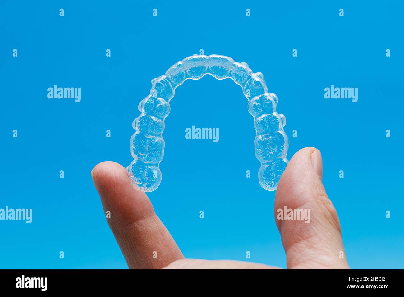 Main tenant un dispositif de retenue transparent sur fond bleu.Concept d'orthodontie Invisalign Banque D'Images