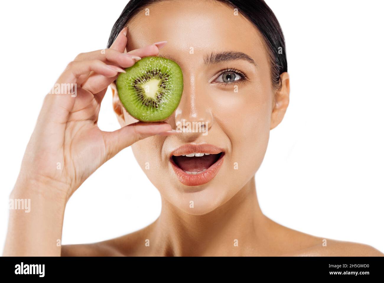 Surprise jeune femme choquée tenant le kiwi devant ses yeux, belle femme avec une tranche de kiwi sur fond blanc, fruits tropicaux, nourriture saine, B Banque D'Images