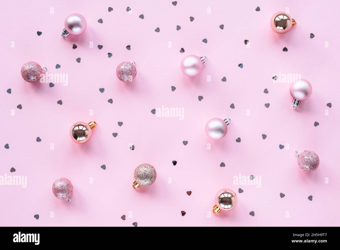 Boules de Noël à fond de fête rose avec confetti en forme de coeur, vue du dessus.Pose à plat Banque D'Images