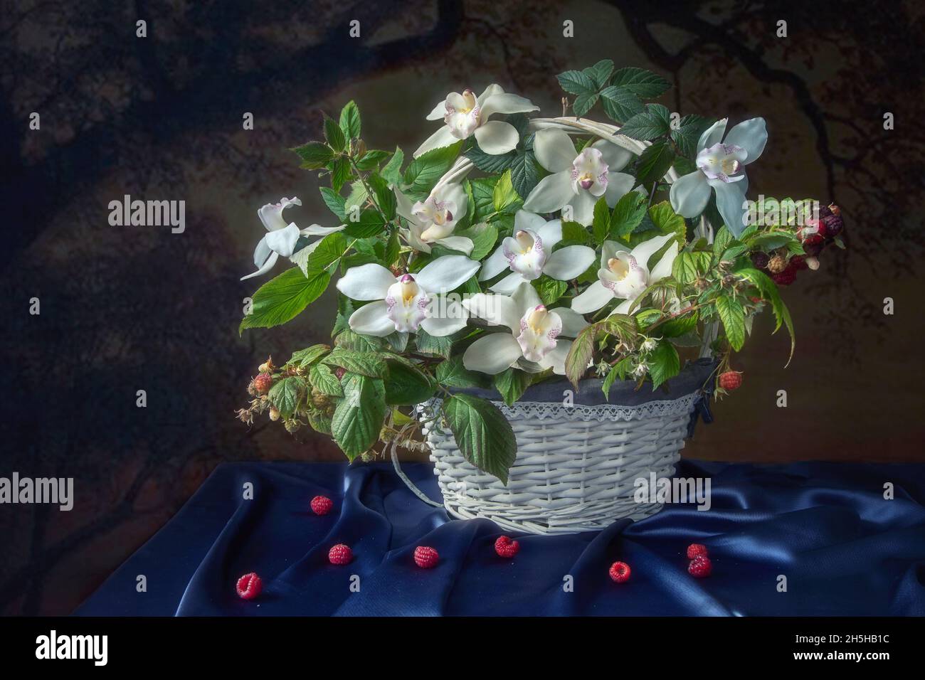 Encore la vie avec un panier de branches de framboises et de fleurs d'orchidées Banque D'Images