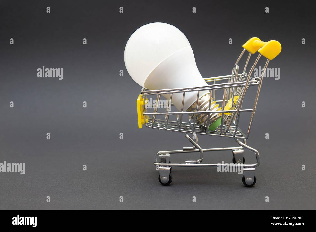 Ampoule LED dans un panier miniature sur fond gris.Concept d'économie d'énergie. Banque D'Images