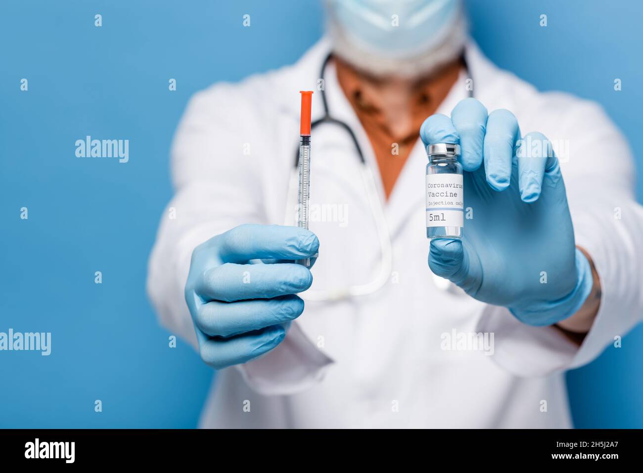 vue rognée du médecin dans des gants en latex tenant le flacon avec le vaccin coronavirus et la seringue isolée sur le bleu Banque D'Images