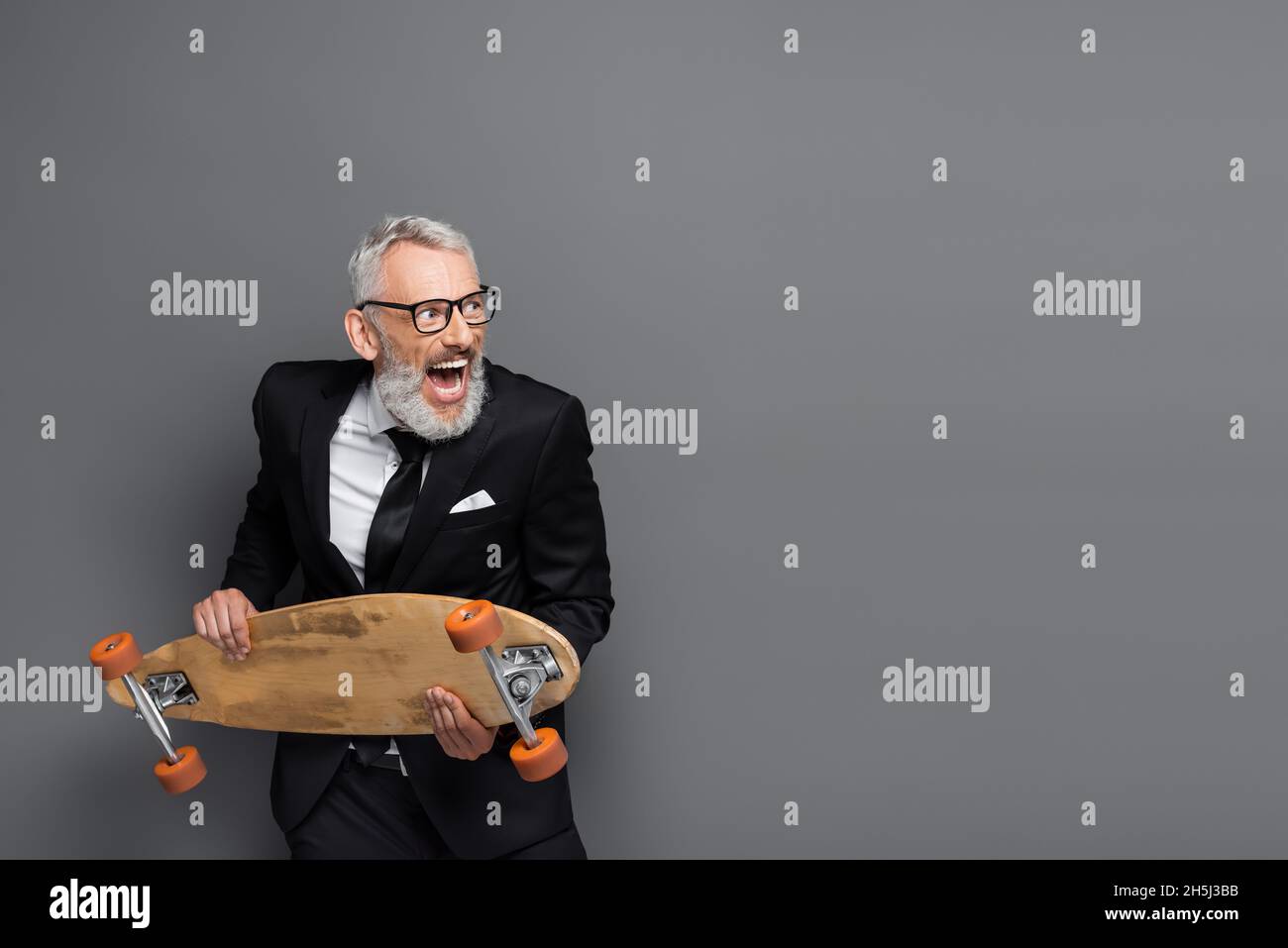 homme d'affaires d'âge moyen en costume et lunettes tenant la planche de bord et criant sur le gris Banque D'Images