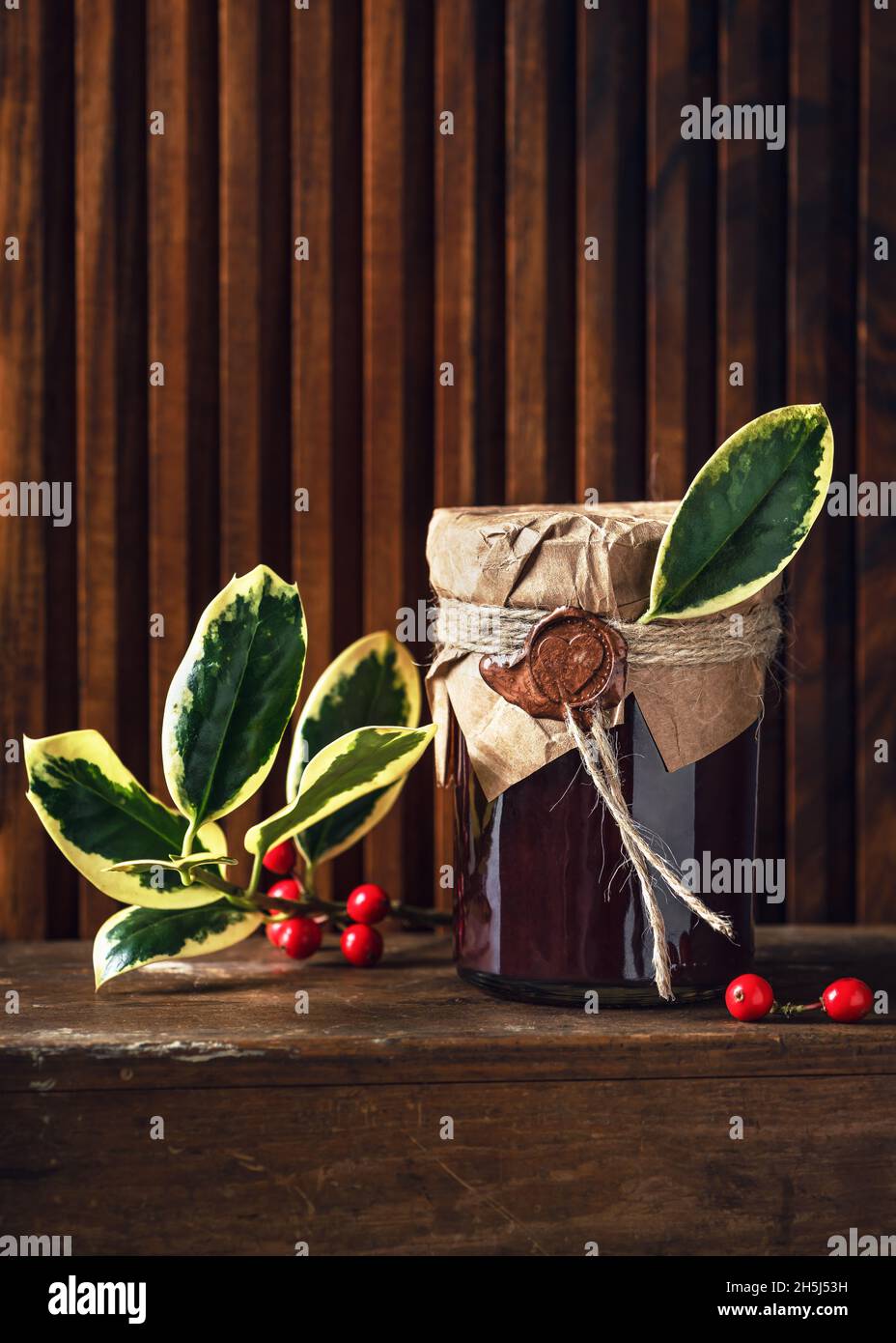 Confiture de fruits maison dans un pot décoré avec du papier de grunge, du sceau de cire et des feuilles vertes de houx comme petit cadeau de Noël. Concept d'idées de cadeau de cuisine Banque D'Images