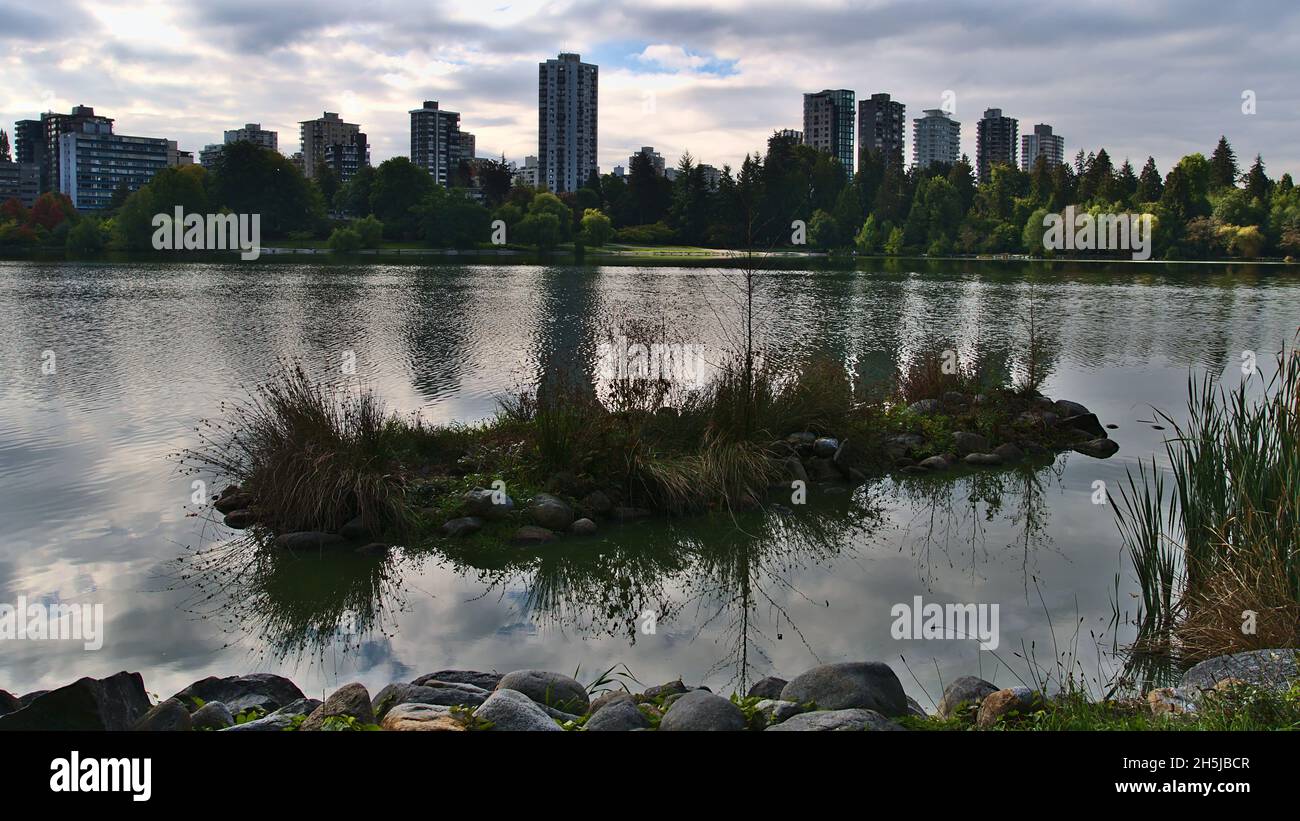 Belle vue sur le petit lac Lost Lagoon dans le parc Stanley avec la ligne d'horizon du quartier Westend à Vancouver, Colombie-Britannique, Canada par temps nuageux. Banque D'Images