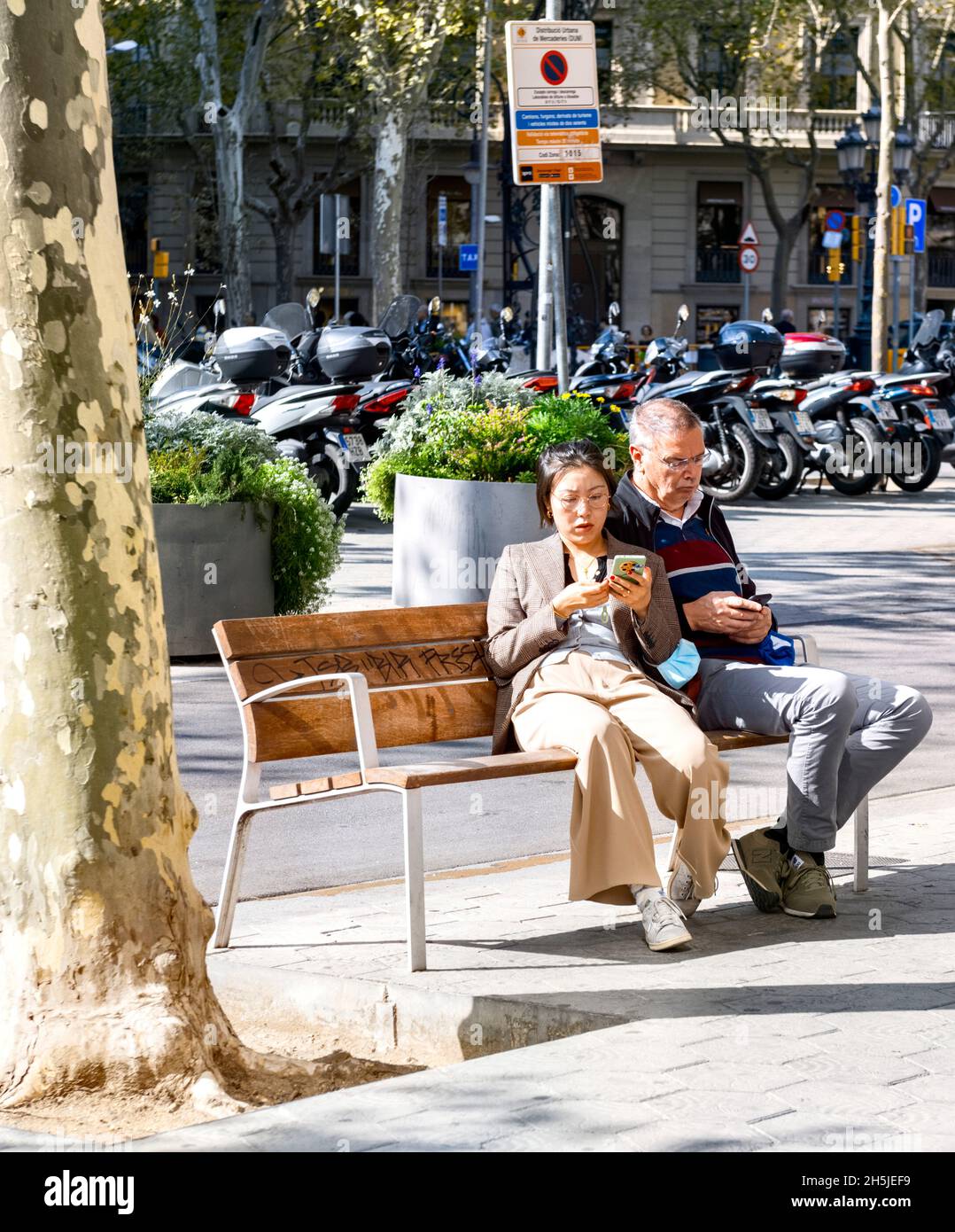 Homme et femme assis sur le banc pour regarder leurs téléphones mobiles, Barcelona Spain Passeig de Gracia Banque D'Images