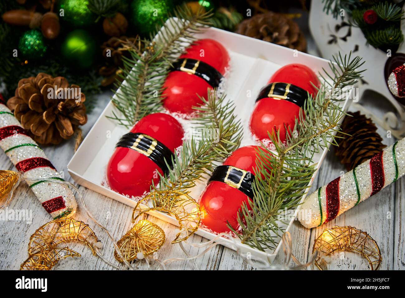 Dessert de Noël rouge sous forme de mousse sur fond de bougies, guirlandes, branches de sapin et cônes Banque D'Images