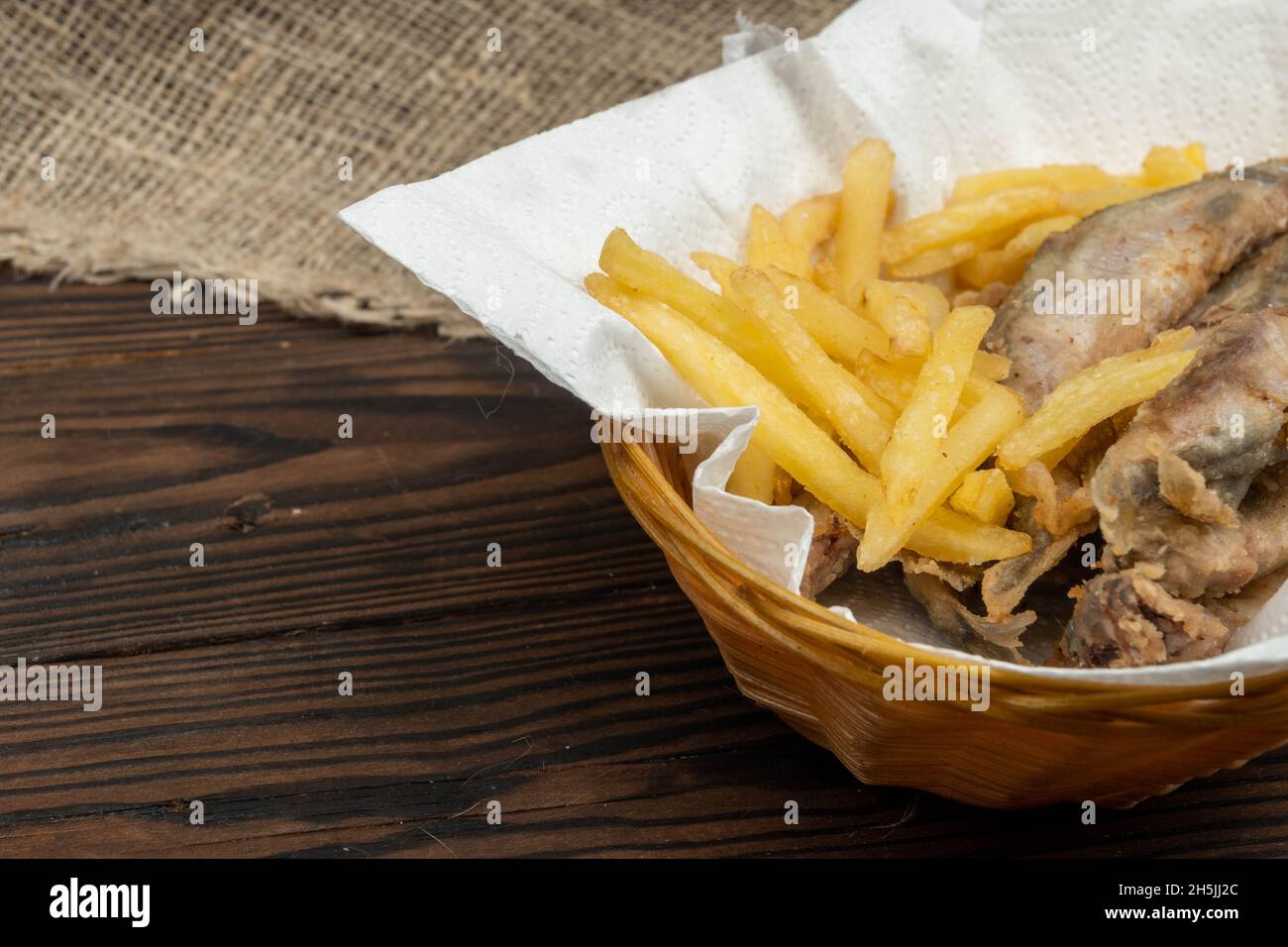 Poisson frit et frites sur une serviette en papier dans un panier en osier sur une table en bois Banque D'Images
