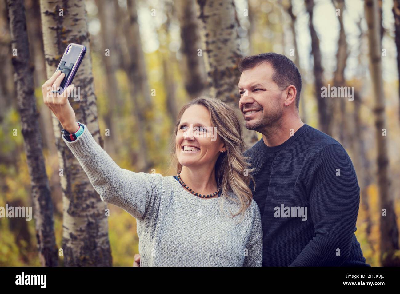 Un couple marié passe du temps ensemble à l'extérieur dans un parc de la ville pendant un après-midi d'automne chaud, en prenant un auto-portrait avec un téléphone intelligent Banque D'Images