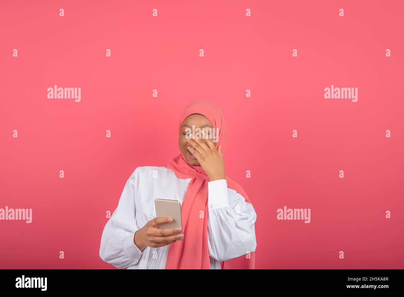 jeune femme musulmane africaine souriant tout en utilisant son téléphone isolé sur fond rose Banque D'Images