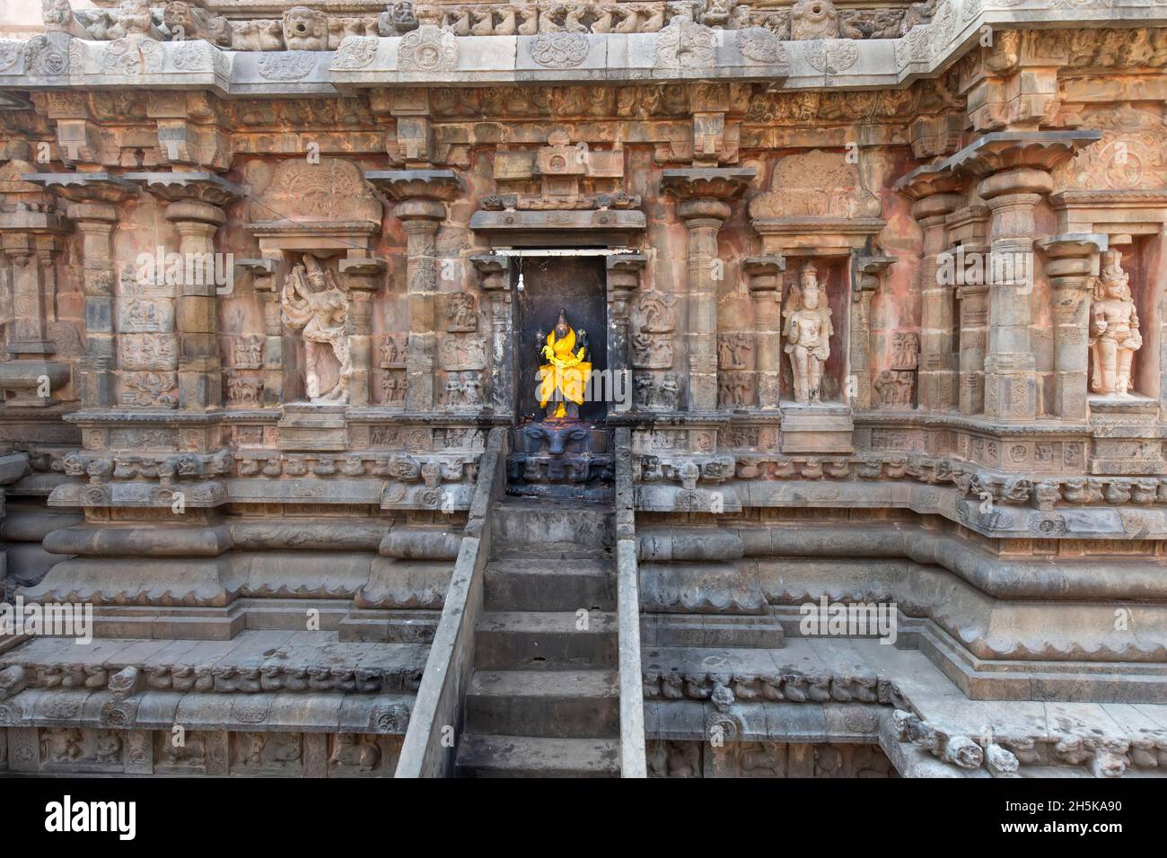 Escaliers menant à une alcôve avec une statue de la divinité hindoue enveloppée de soie jaune vif dans un mur de pierre du temple Dravidian Chola de l'ère Airavatesvara Banque D'Images