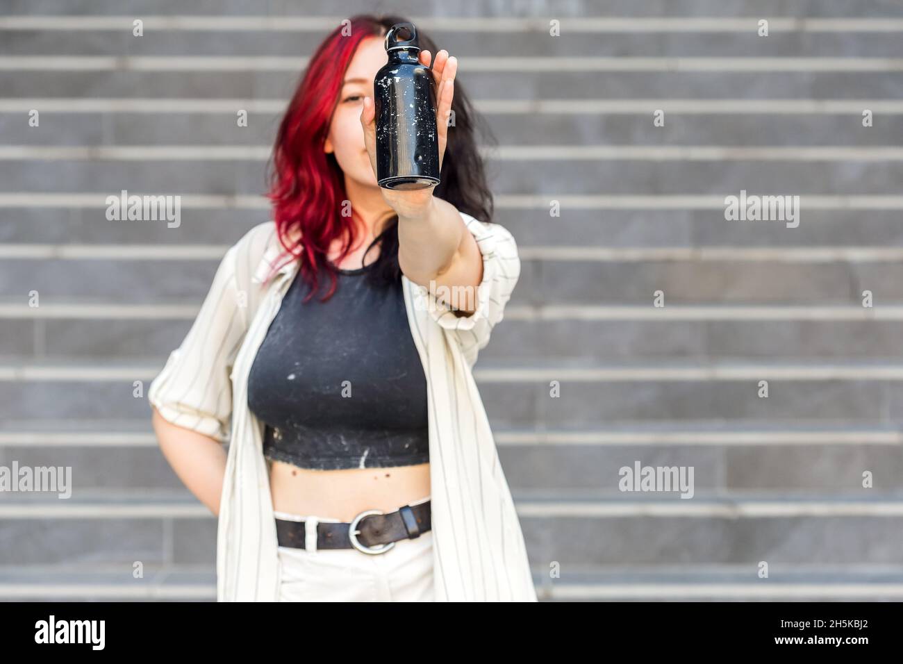 Belle jeune femme montrant une vieille bouteille d'eau réutilisable en acier inoxydable sur fond gris.Consumérisme durable, concept réutilisable sans plastique Banque D'Images