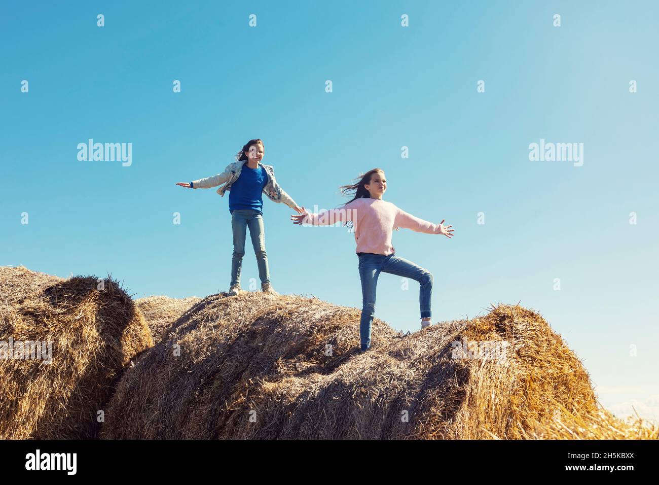 Deux jeunes sœurs jouant sur une pile de balles de foin; Alcomdale, Alberta, Canada Banque D'Images
