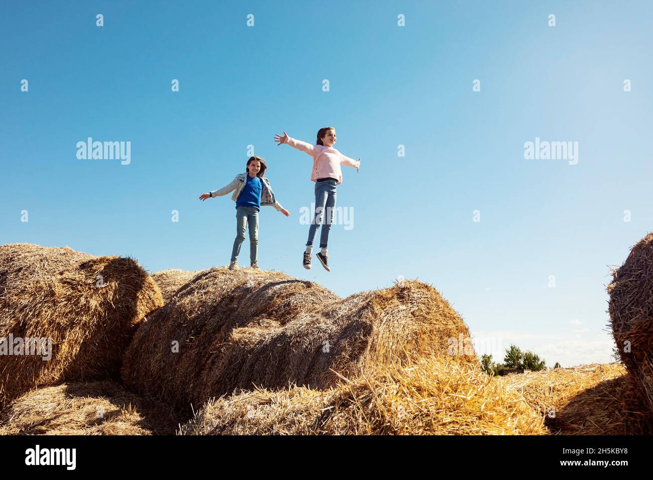 Deux jeunes sœurs jouant sur une pile de balles de foin; Alcomdale, Alberta, Canada Banque D'Images