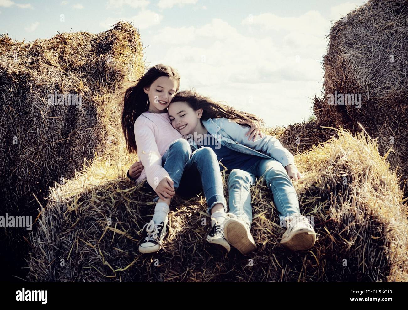 Deux jeunes sœurs passent du temps ensemble pendant qu'elles sont assises sur des balles de foin dans leur ferme familiale; Alcomdale, Alberta, Canada Banque D'Images