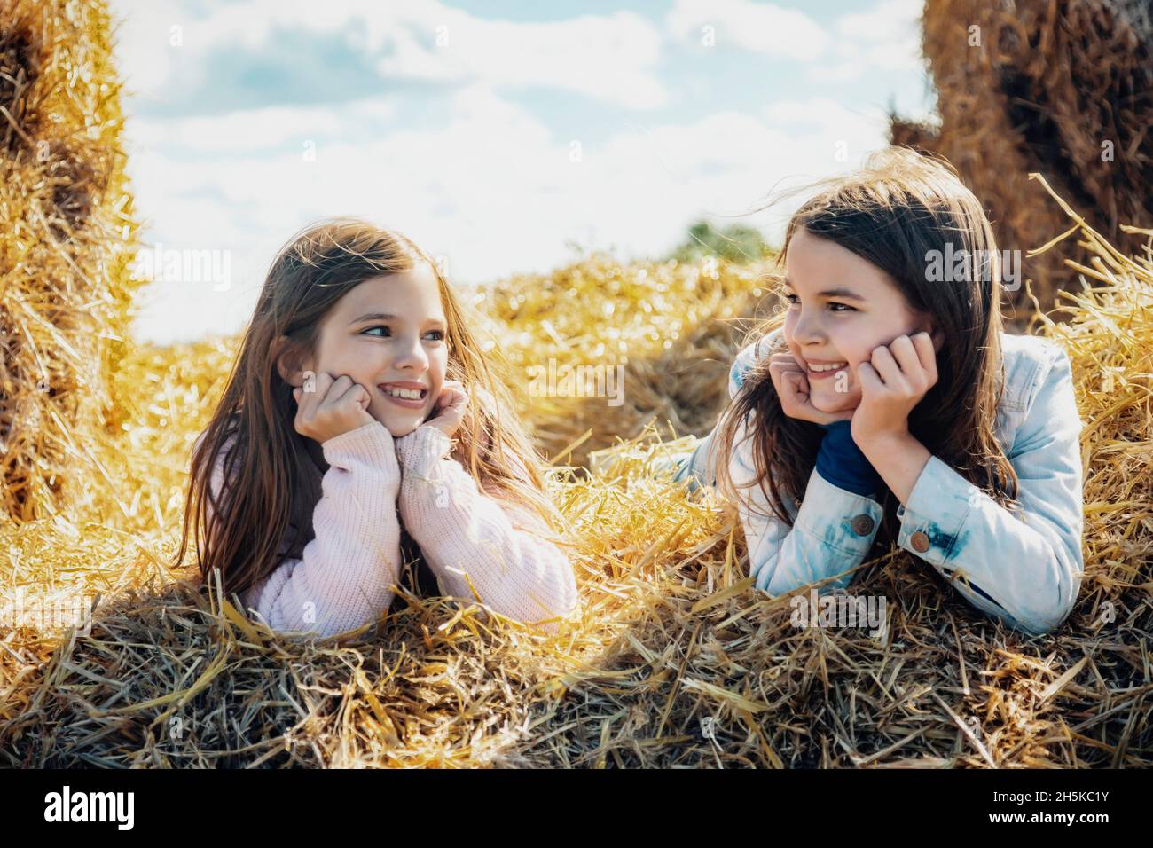Deux jeunes sœurs passent du temps ensemble de qualité tout en étant allongé sur des balles de foin dans leur ferme familiale; Alcomdale, Alberta, Canada Banque D'Images