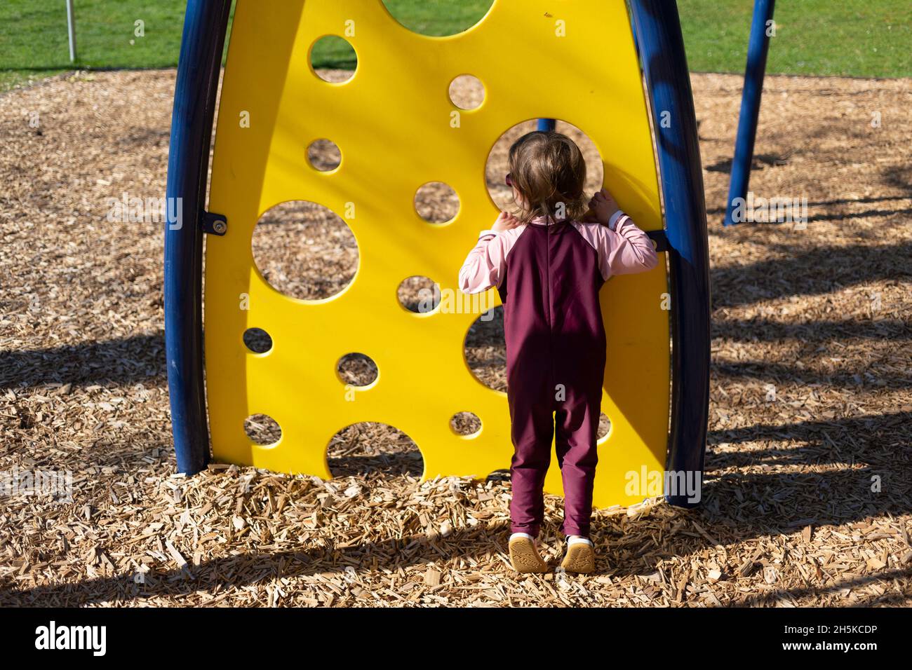 Une jeune fille d'âge préscolaire regarde à travers un trou d'une structure de jeu dans un terrain de jeu; North Vancouver, Colombie-Britannique, Canada Banque D'Images