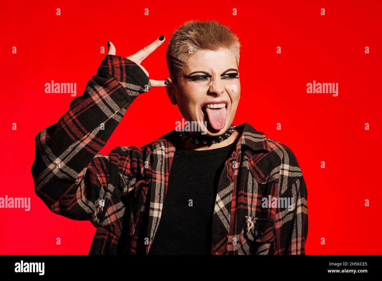 Cheveux courts blonde rock fille montrant sa langue sur un fond rouge Banque D'Images