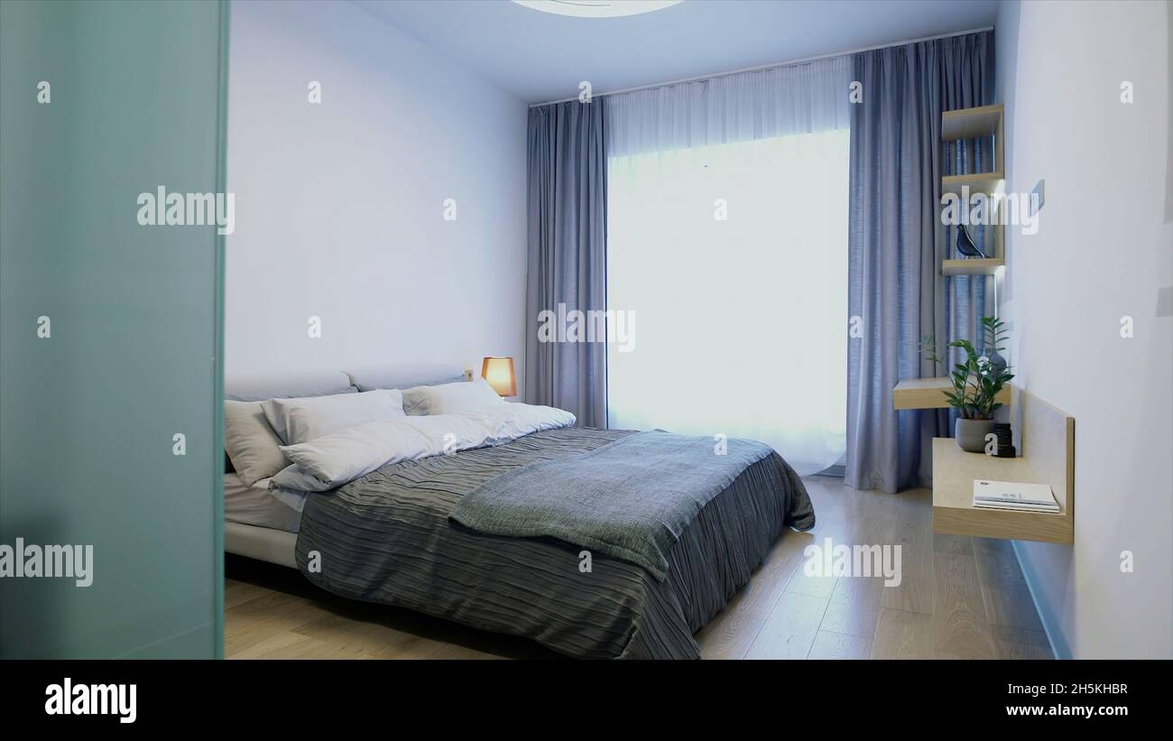 Nouvelle chambre d'hôtel avec une chambre pleine de lumière du soleil.Vidéo.Bel intérieur avec un lit double, une lampe, une grande fenêtre et des étagères au mur Banque D'Images