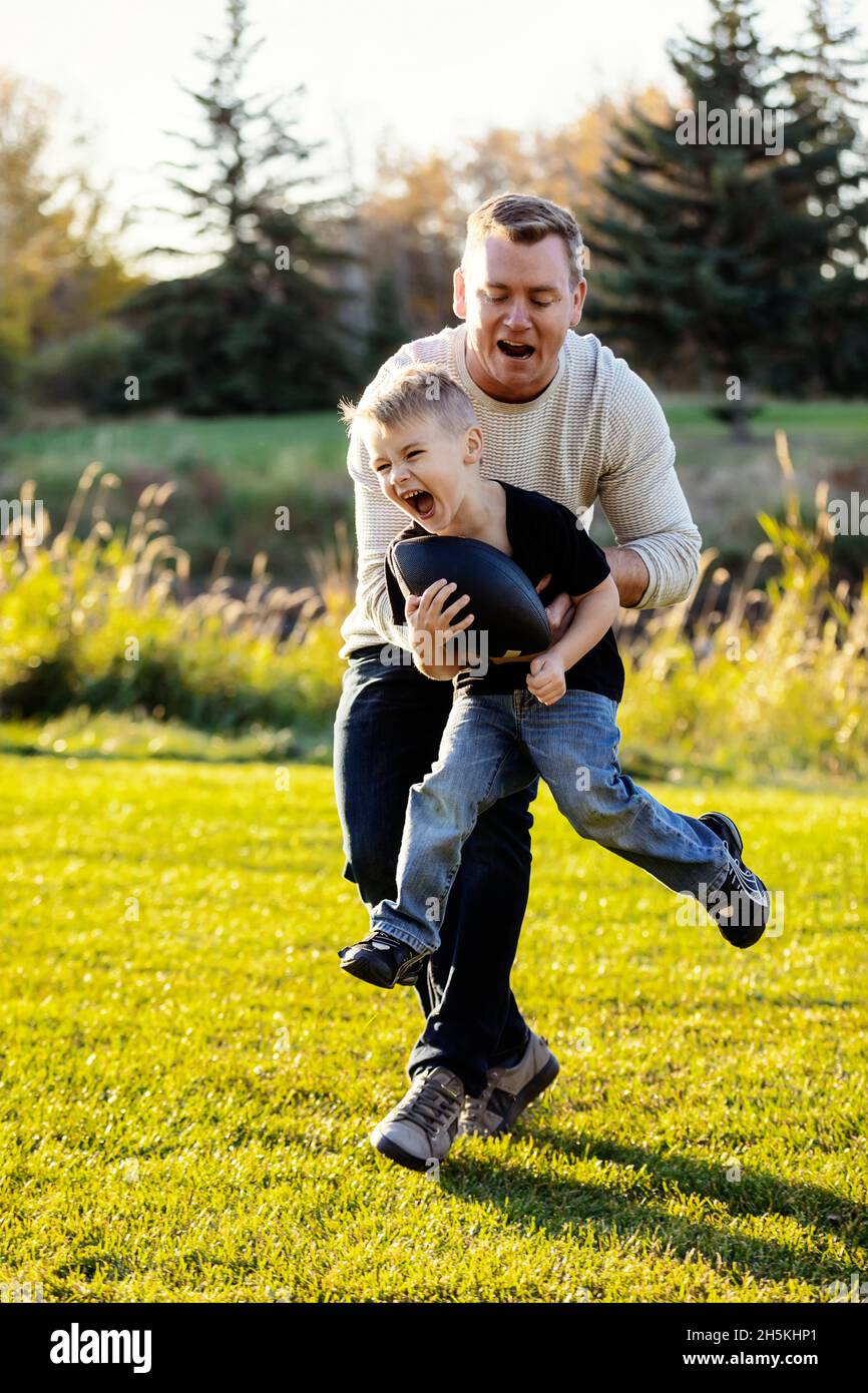 Père jouant au football avec son jeune fils dans un parc en automne; St. Albert, Alberta, Canada Banque D'Images