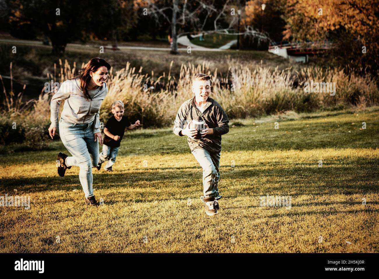 Mère pourchassant son fils dans une partie de football lors d'une belle journée d'automne dans un parc de la ville; St. Alberta, Alberta, Canada Banque D'Images