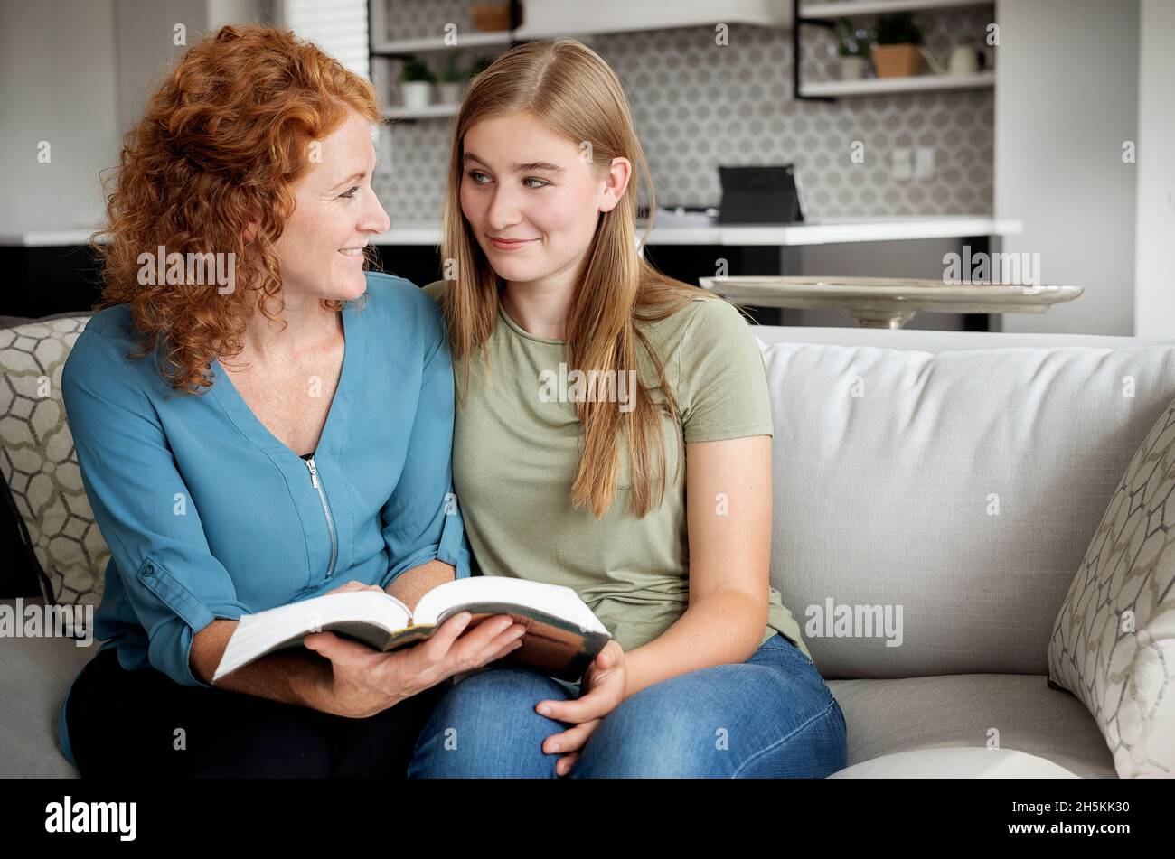 Mère et fille adolescente assises sur un canapé à la maison lisant la Bible ensemble; Edmonton, Alberta, Canada Banque D'Images