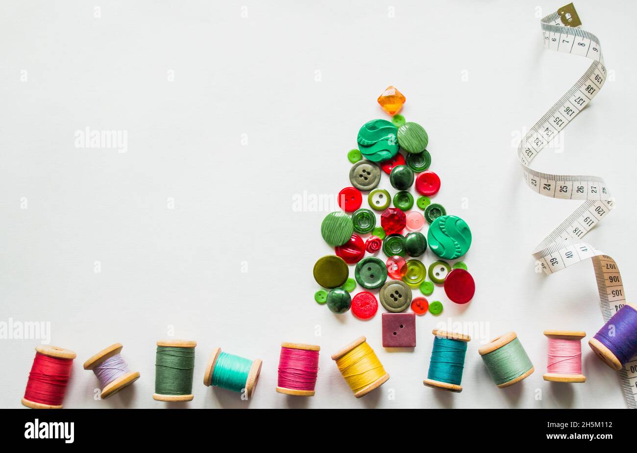 Un arbre de Noël en boutons vert, rouge.Fils multicolores avec bobines en bois, ruban de mesure.Arrière-plan blanc, espace de copie.Chr. Créatif Banque D'Images