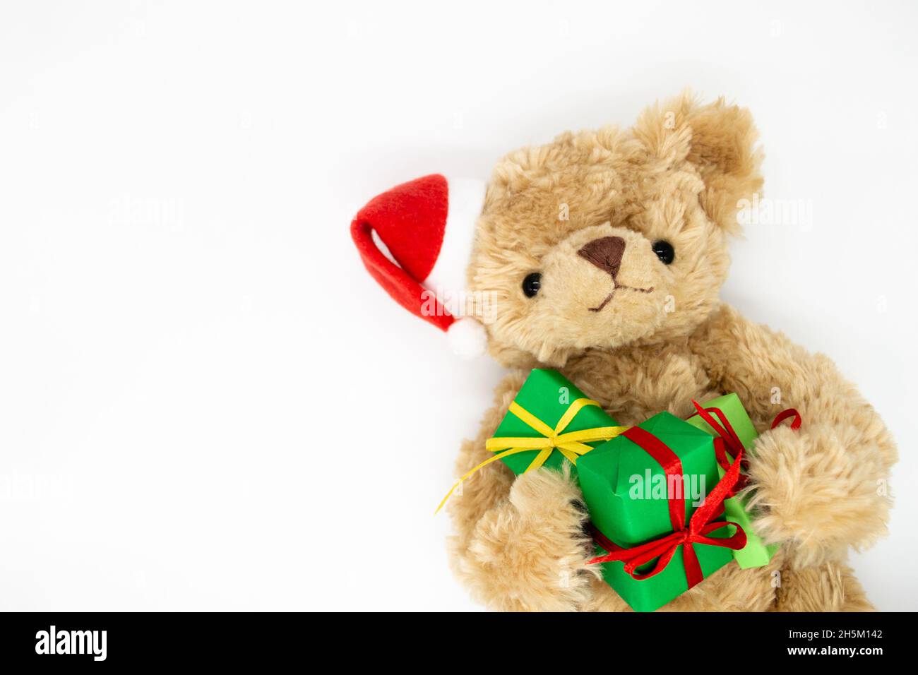 Un ours en peluche Teddy dans un chapeau de Père Noël rouge avec pompon sur une oreille, tenant des boîtes-cadeaux vertes dans ses pattes.Arrière-plan blanc, espace de copie.Le co Banque D'Images
