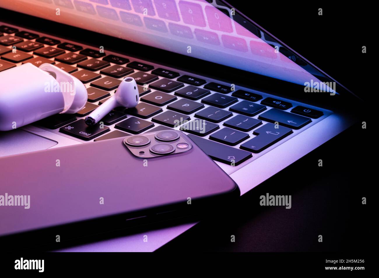 un ordinateur portable à moitié fermé dans l'obscurité avec un téléphone et des écouteurs sans fil lumineux Banque D'Images