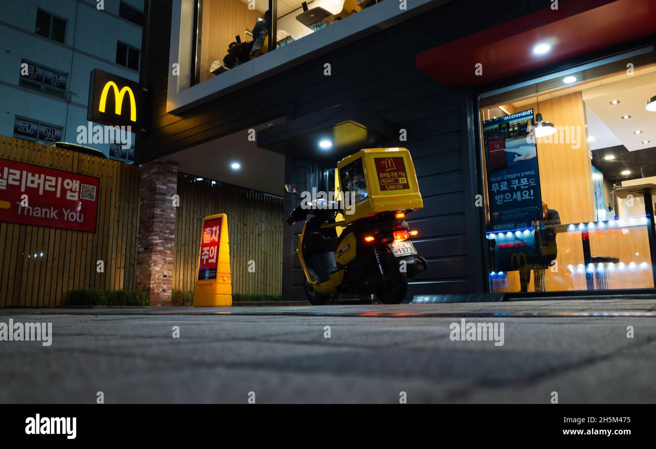 Busan, Corée du Sud - 19 mars 2018: Rue de nuit avec, livraison de scooter stands à l'entrée du restaurant de restauration rapide McDonalds Banque D'Images