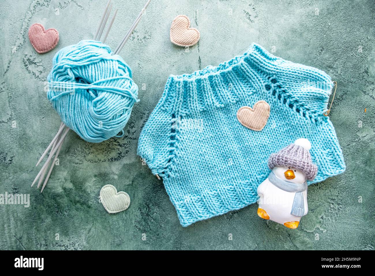 Le concept de tricotage des vêtements pour les jouets et les bébés.T-shirt tricoté en fil de coton turquoise.Une boule de fils, aiguilles de tricotage, jouet et velours Banque D'Images