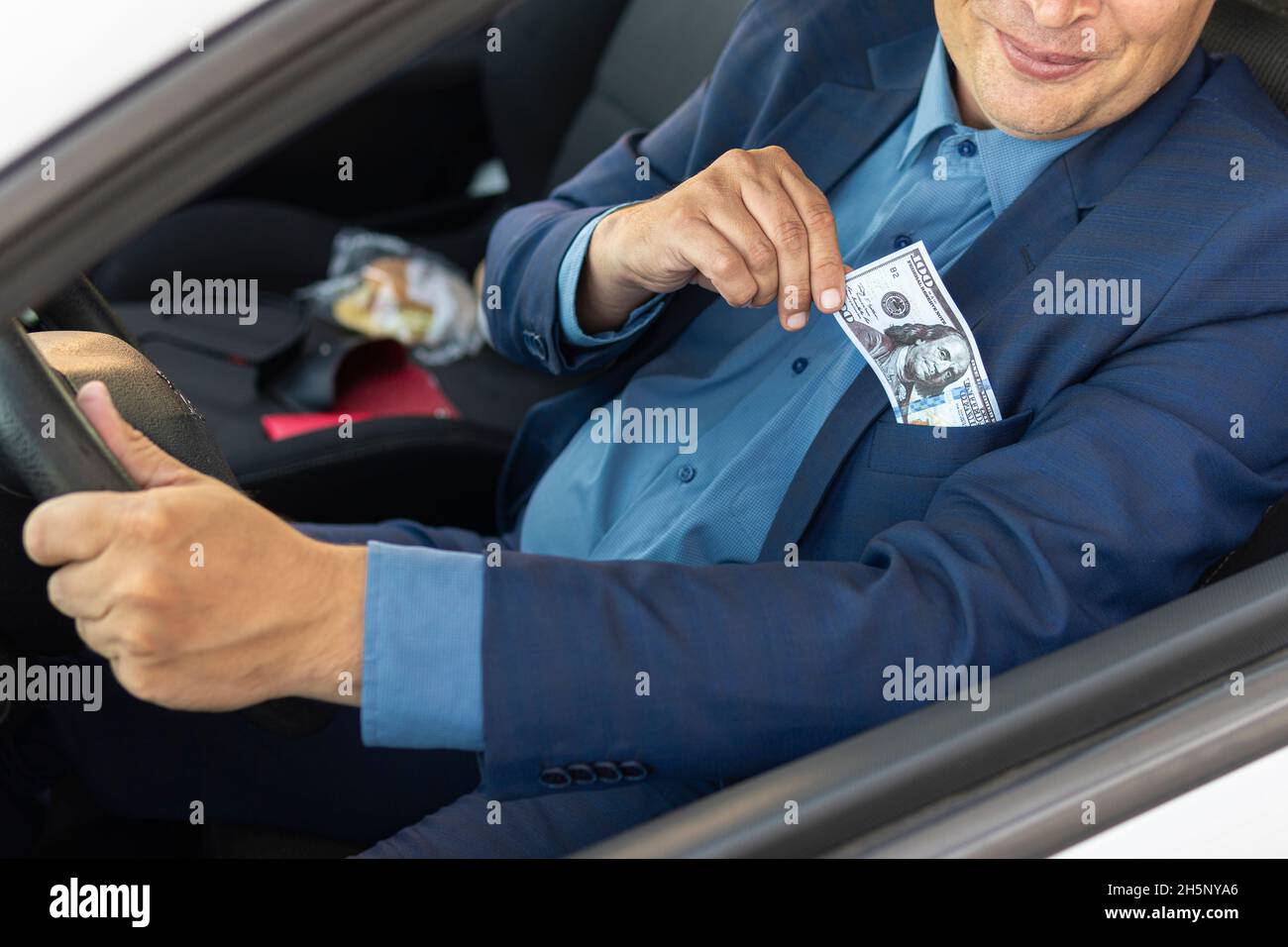 Le conducteur, un homme en costume cher, sort 100 dollars de sa poche.Le concept de corruption sur les routes.Un député donne un pot-de-vin à un corrup Banque D'Images