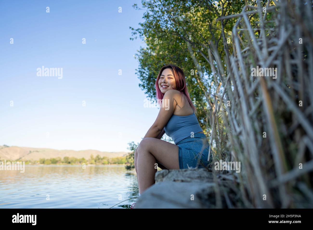 Jeune femme asiatique à Dappled lumière du soleil assis sur la rive d'un lac idyllique Banque D'Images