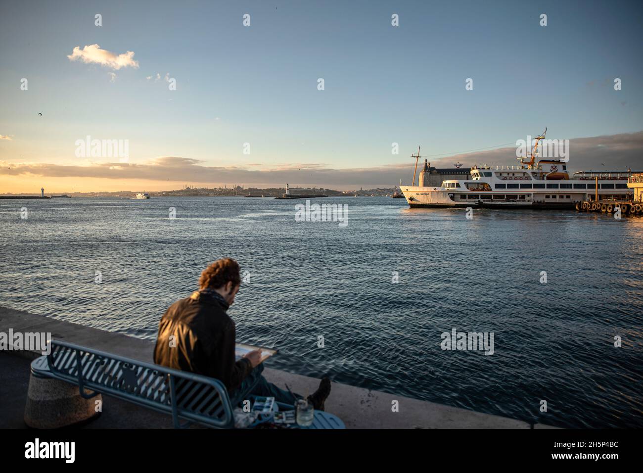 Istanbul, Turquie.10 novembre 2021.Un homme vu assis sur un banc alors que le ferry des lignes de la ville part de la jetée.Crédit : SOPA Images Limited/Alamy Live News Banque D'Images