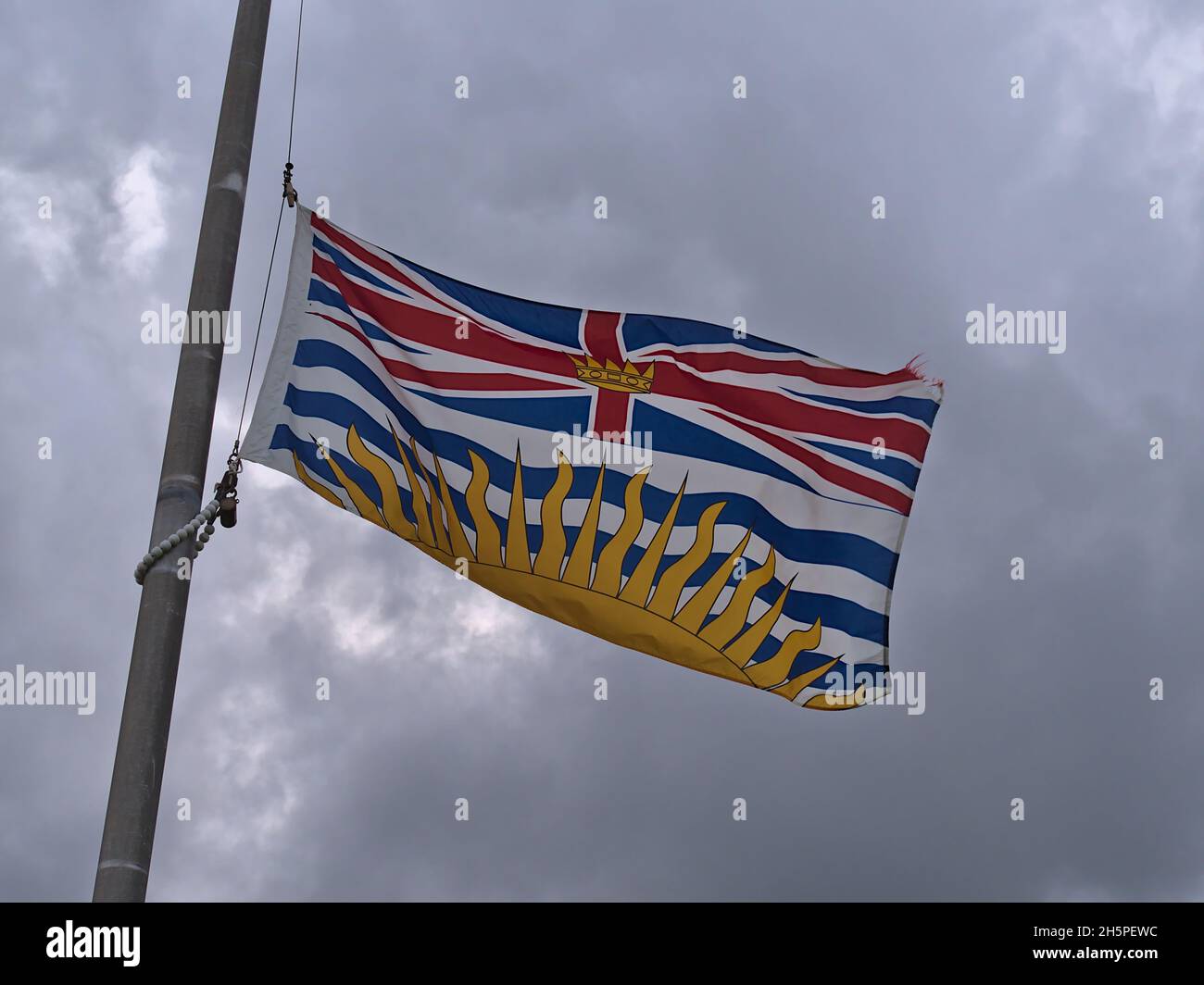 Drapeau provincial de la Colombie-Britannique avec couronne au centre du drapeau royal de l'Union et coucher du soleil sur le mât à Port Hardy, Canada. Banque D'Images