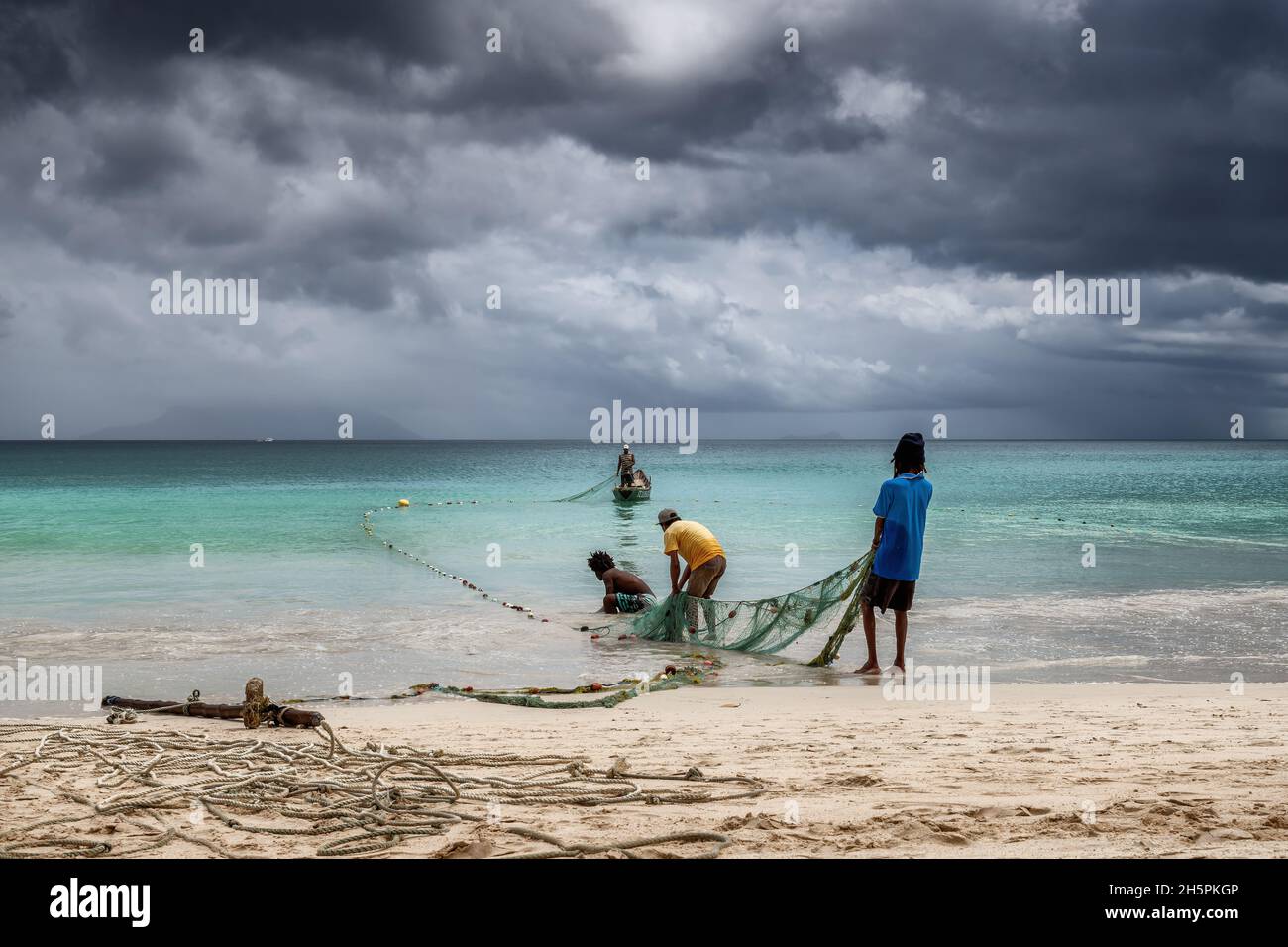 Les pêcheurs tirent des filets de la mer sur une plage sous les tropiques avec un ciel spectaculaire sur l'île de Mahé, aux Seychelles Banque D'Images