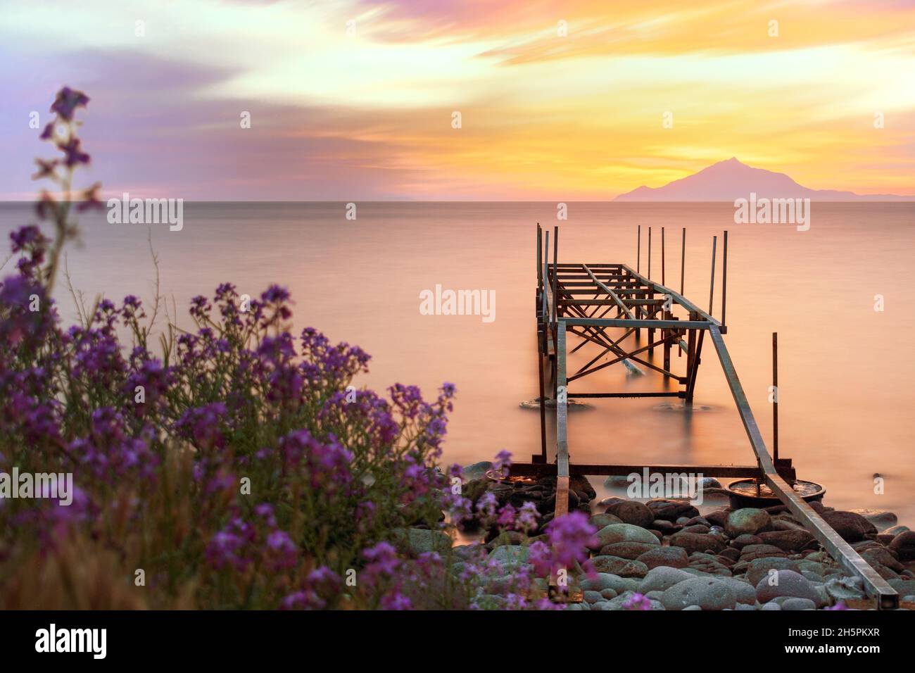 Coucher de soleil sur la mer avec un fond de Mont Athos et une jetée sur une plage Banque D'Images