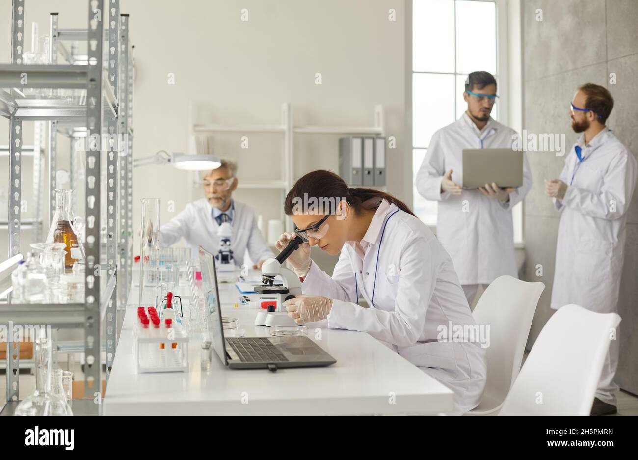 Une jeune femme intelligente examine des échantillons d'essai au microscope dans un laboratoire médical moderne. Banque D'Images