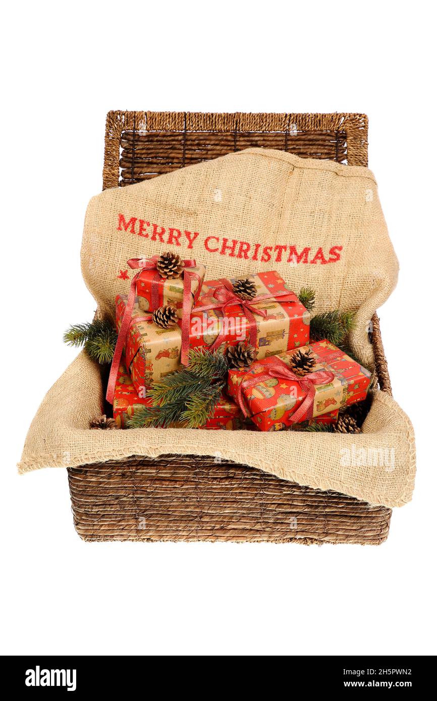 Cadeaux de Noël emballés avec rubans rouges sur un sac de jute avec texte « Joyeux Noël », décoré avec des cônes de pin et des brindilles de pin dans un panier en osier, isol Banque D'Images