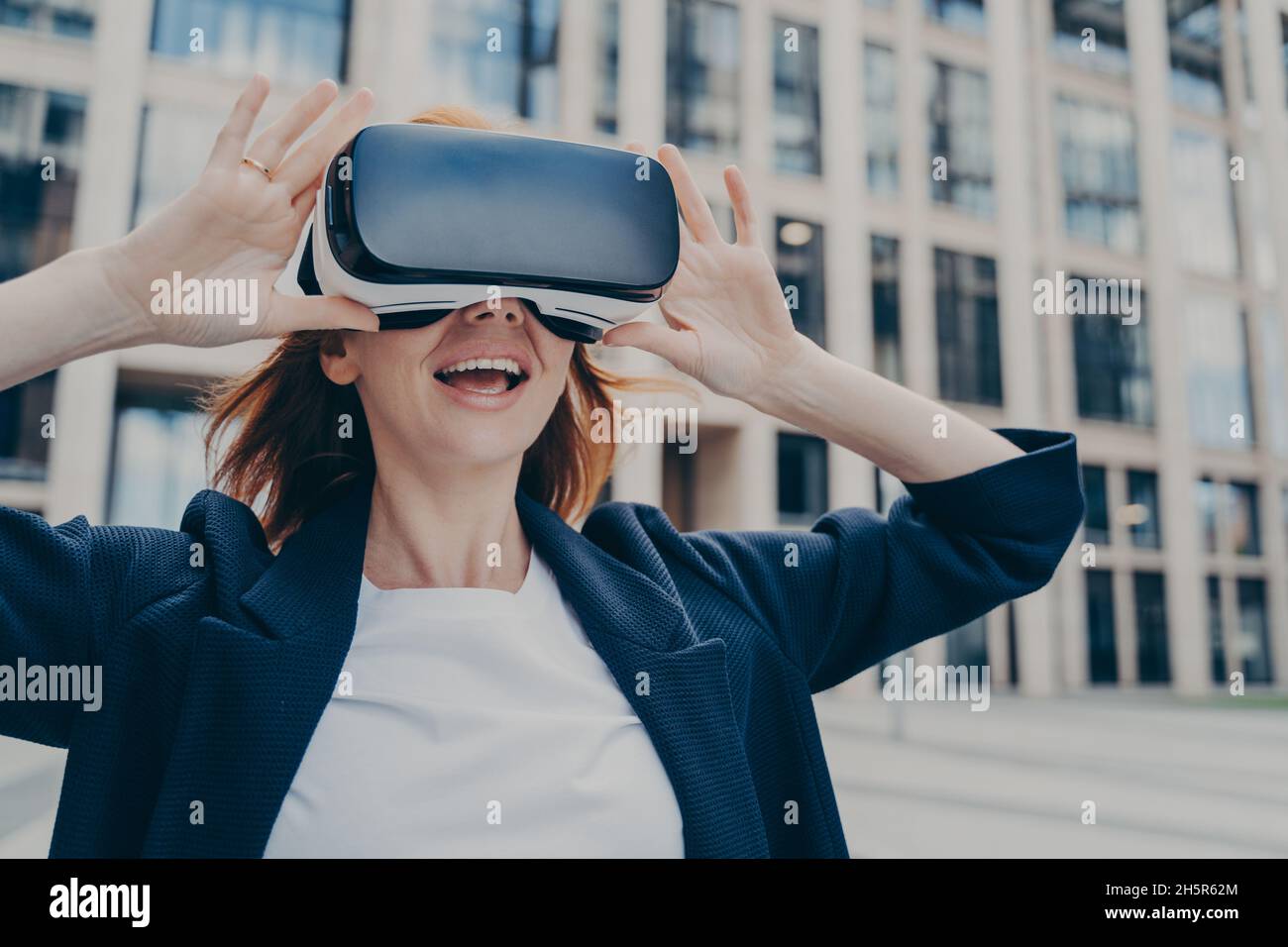 Femme d'affaires excitée explorant la réalité virtuelle avec un casque VR en extérieur Banque D'Images