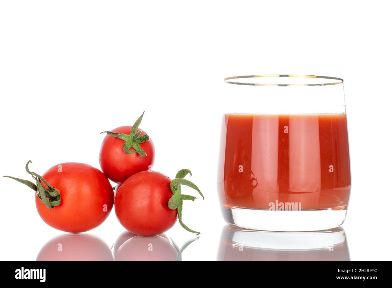 Une tasse en verre avec jus de tomate et trois tomates, en gros plan, isolées sur du blanc. Banque D'Images