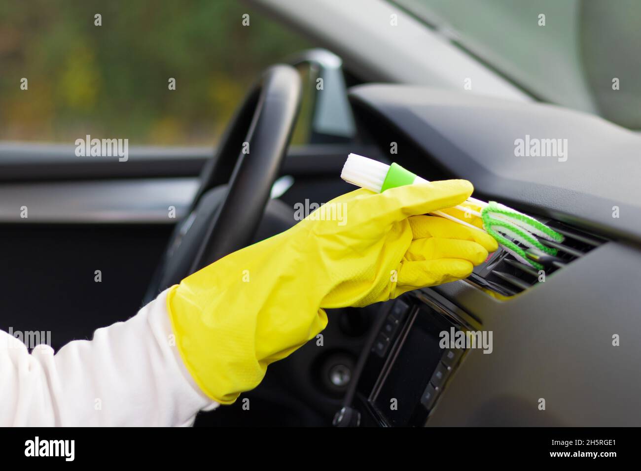 Une main dans des gants en caoutchouc jaune essuie le tableau de bord d'une voiture de la poussière avec une brosse spéciale lors d'un jour d'automne brillant.Mise au point sélective.Gros plan Banque D'Images