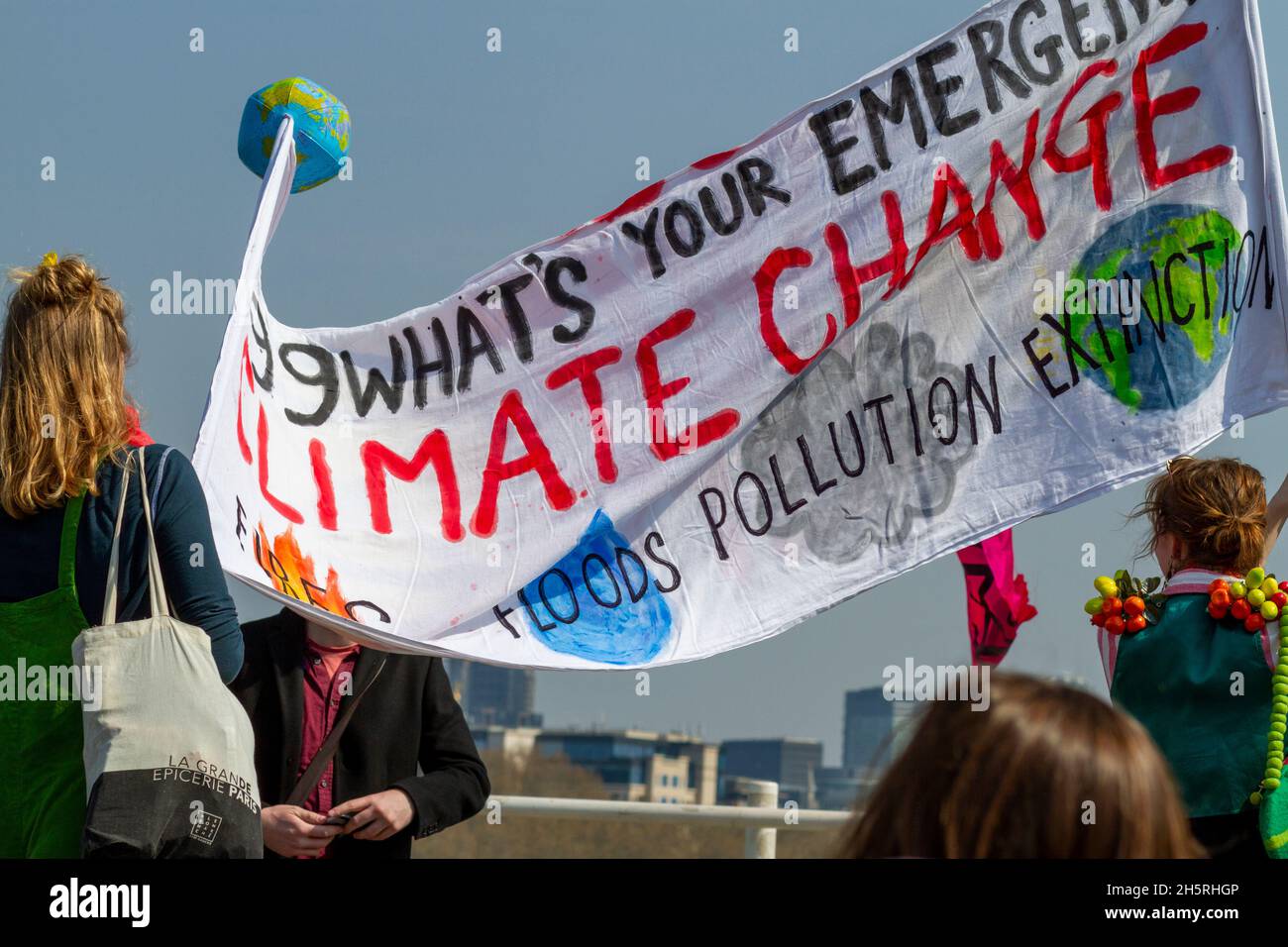 Photographie de rue d'un groupe de manifestants du changement climatique avec une grande bannière maison avec dos à la caméra.Certains bâtiments sont visibles derrière. Banque D'Images