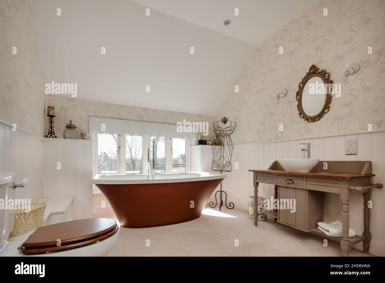 Suffolk, Angleterre - Mars 2018: WC de salle de bains avec bassin en céramique sur plinthe en bois, demi-murs en bois et baignoire sur pied. Banque D'Images