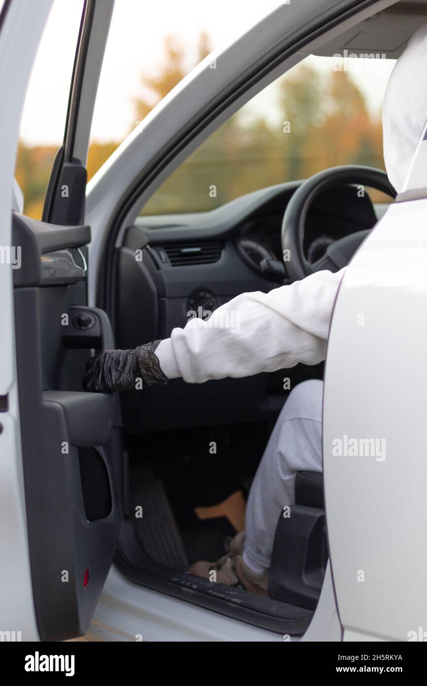 Un homme dans un chandail blanc avec une capuche s'assoit au volant d'une voiture et essaie de la démarrer afin de la voler.Mise au point sélective.Gros plan Banque D'Images
