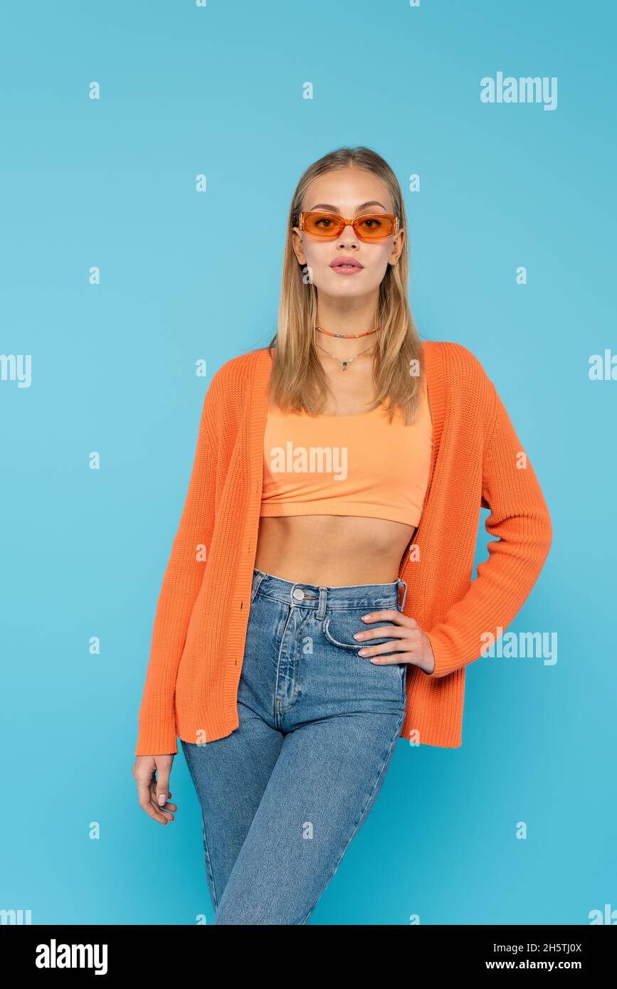 Femme blonde en lunettes de soleil tenant la main sur la hanche isolée sur le bleu Banque D'Images