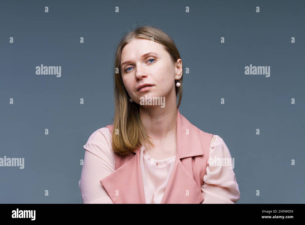 Femme modeste et naïve aux cheveux blonds, élégamment vêtue de veste et de chemise roses, heureux.Studio photo de belle jolie femme isolée sur le fond de mur vide de studio. Banque D'Images