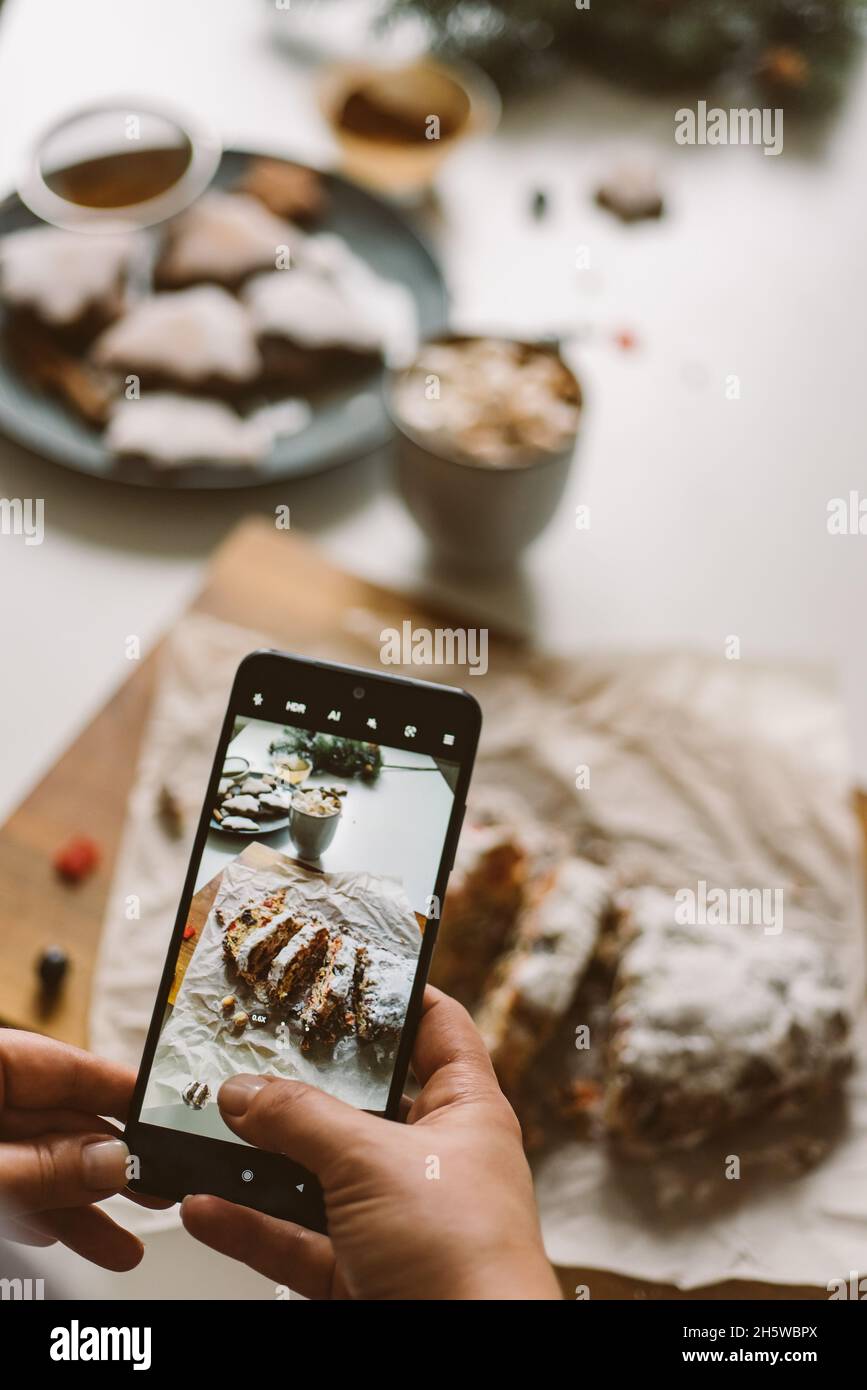 Le boulanger prend une photo du stollen de Noël cuit, sur un téléphone mobile foyer sélectif, préparation des vacances, l'esprit de noël vertical Banque D'Images