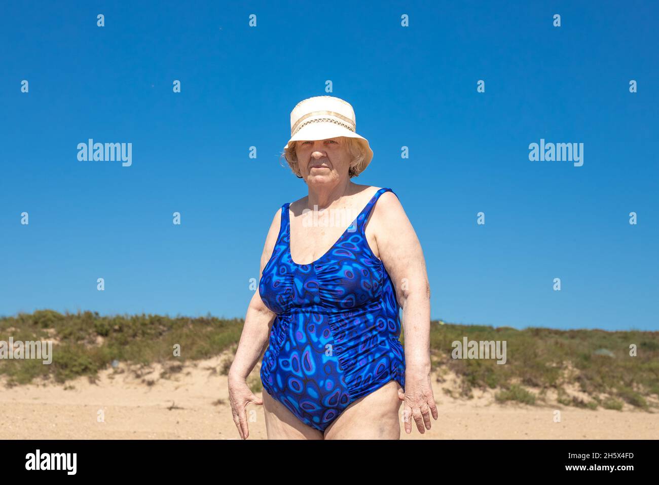 Une femme âgée en maillot de bain et chapeau bleus se tient sur le bord de  mer, sur fond de ciel bleu.Repos marin à la retraite Photo Stock - Alamy